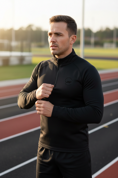 Man adjusting his black athletic jacket on a track field during sunset.