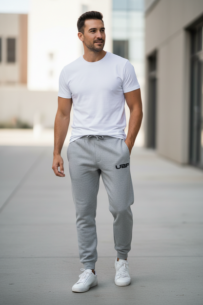 Man wearing a white t-shirt and gray jogger pants with a brand logo, standing on a sidewalk.