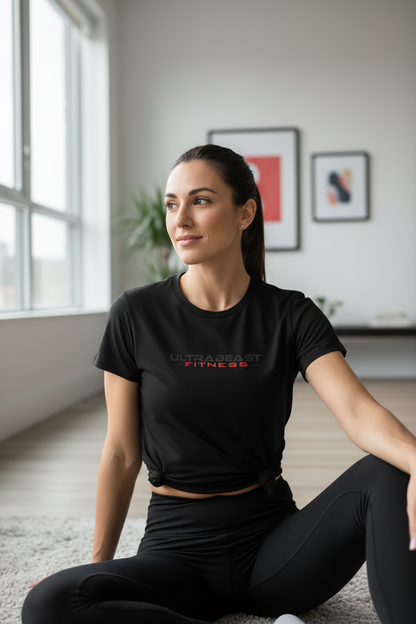 Woman sitting on the floor wearing a black 'Ultra Beast Fitness' t-shirt in a room with large windows.